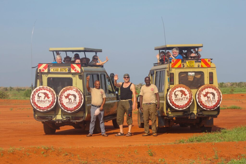 Guests and Mbutu guides beside two Mbutu Land Cruisers