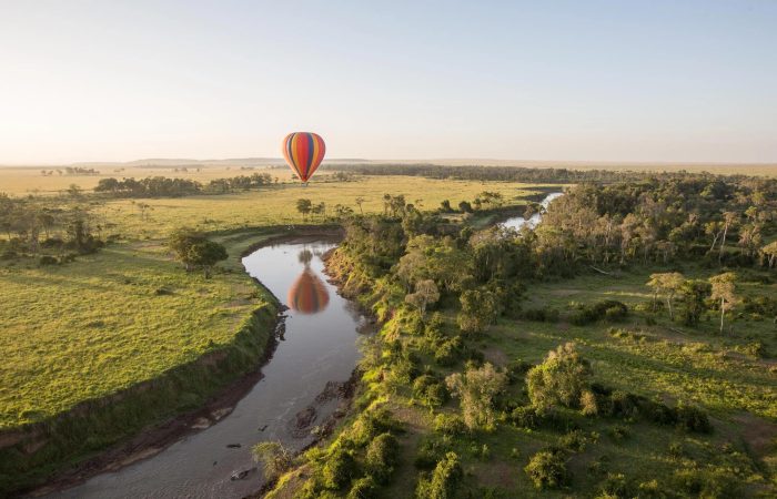 Luxury hot air balloon safari at sunrise over the Maasai Mara with wildlife roaming below.