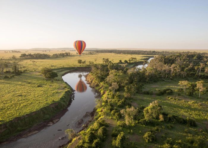 Luxury hot air balloon safari at sunrise over the Maasai Mara with wildlife roaming below.